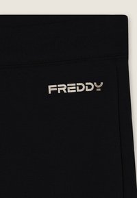 Leggings negros con una textura suave y una cinturilla elástica, con un logotipo metálico plateado "FREDDY" impreso en el lateral.