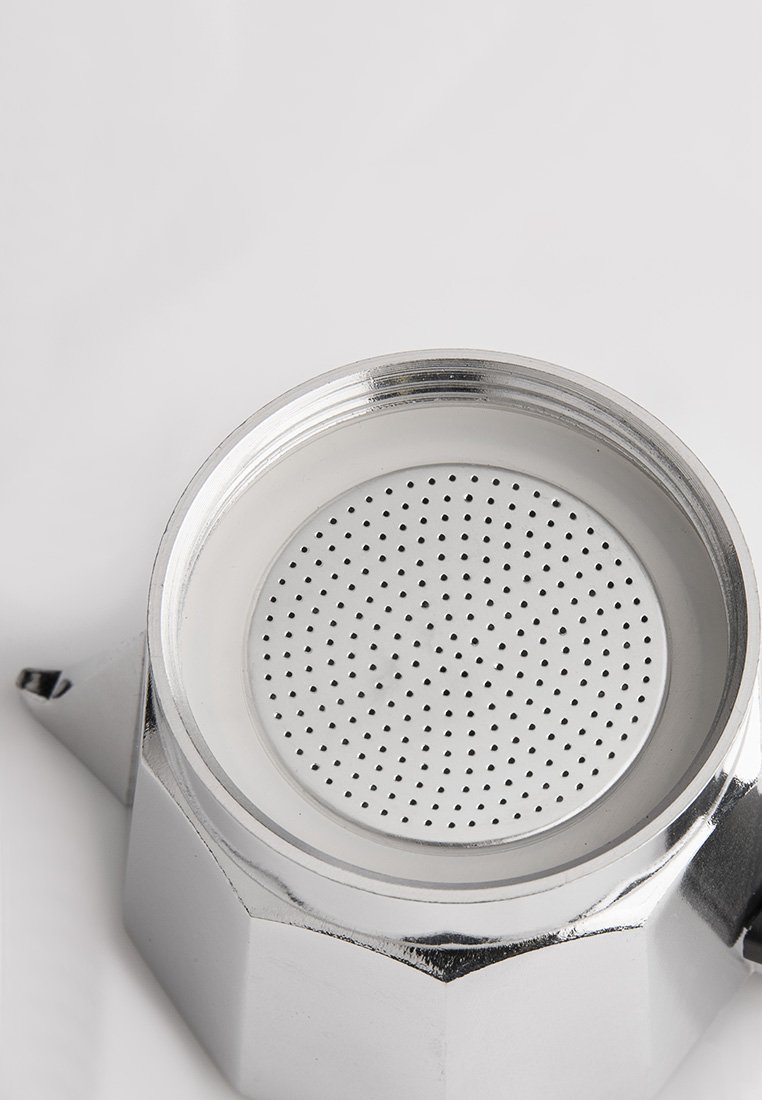 Draufsicht auf eine silberne, metallene Espressokanne mit kleinen kreisförmigen Löchern auf der Filterplatte im Inneren.