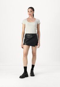 Camiseta gris ajustada de manga corta, combinada con una minifalda negra de cuero sintético, calcetas negras y zapatos negros gruesos. Accesorios mínimos.