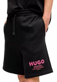 Czarne szorty z polaru z elastycznym pasem i sznurkiem. Wyraźny różowy napis logo na dolnej lewej nodze. Miękka faktura.