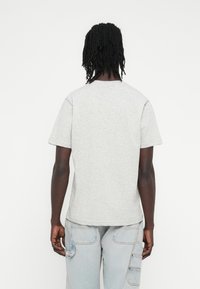 Grey cotton t-shirt with short sleeves, round neckline, relaxed fit, textured fabric, and a straight hem, worn with light blue cargo pants.