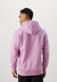 Ροζ φούτερ με κουκούλα, με ριμπ μανσέτες και στρίφωμα, φτιαγμένο από μαλακό ύφασμα. Φορεμένο ανάποδα, δείχνει την κουκούλα και τις καθαρές γραμμές.