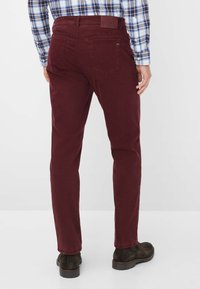 Pantaloni dritti color borgogna in cotone, con tasche posteriori, un'etichetta in pelle sulla vita e indossati con stivali scuri.
