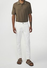 Brązowa koszulka polo z dwoma guzikami, białe akcenty na kołnierzyku, białe spodnie i brązowe sandały na dwóch paskach. Widoczna faktura tkaniny.