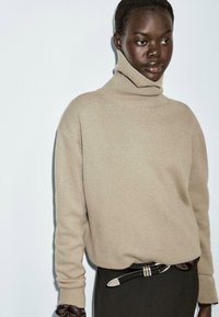 Maglione girocollo beige realizzato in morbido tessuto a maglia, caratterizzato da una vestibilità ampia e dettagli a coste intorno al collo e ai polsini.