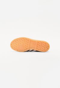 Semelle de sneakers Adidas noir et blanc montrant un motif en nid d'abeille et le logo sur une semelle en caoutchouc translucide.