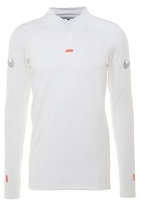 Pitkähihaisen valkoisen suorituspaidan, jossa on korkea kaulus, puoli-vetoketju, teksturoitu kuosi ja harmaa Nike-logo jokaisessa hihassa. Punainen yksityiskohta hihassa.