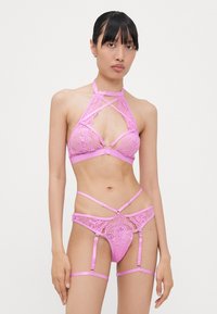 Pink lingerie set with lace inserts, featuring a halter neck design, cross straps, and garter attachments. Soft satin material.