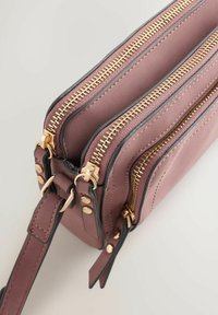 Bolso de cuero rosa con dos compartimentos con cremallera, detalles de herrajes dorados y ribete negro. Cuenta con correa ajustable y detalles cosidos.