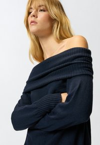 Mornarski pulover s otvorenim ramenima, rebrastom teksturom, dugim rukavima i naboranim izrezom. Mekana tkanina pruža udoban fit.