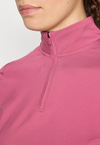 Top atletico fucsia con colletto alto e zip corta, caratterizzato da una texture liscia e elastica e da un minimo di dettagli cuciti.