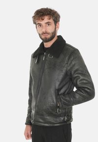 Giubbotto di pelle nera con superficie texturizzata, grande colletto in pelliccia shearling nera, tasche laterali e dettaglio con fibbia in vita.