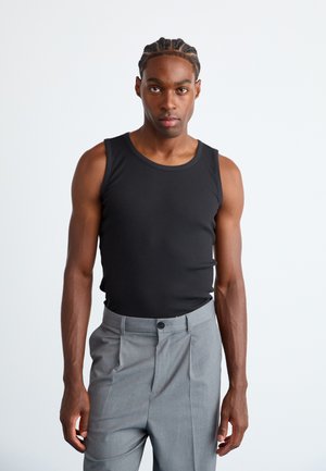 Black ribbed tank top with a round neckline, paired with gray trousers featuring a button and pleated design.