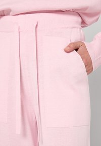 Lichtroze gebreide joggers hebben een elastische tailleband met trekkoord, zijzakken en geribbelde manchetten, met een zachte, gestructureerde afwerking.