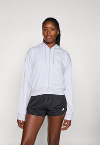 Lys grå hettegenser med glidelås og snøring, ribbede mansjetter og logo på brystet, kombinert med svarte shorts med logo på siden.
