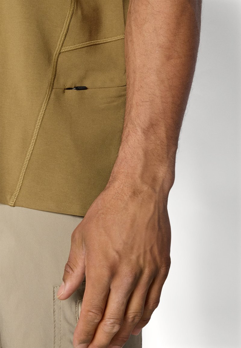 Kortärmad skjorta i olivgrön med texturerad yta, med en liten dragkedjeficka på sidan, samt ljusbeiga byxor med en cargoficka.