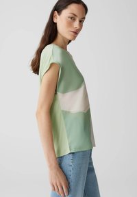 Top verde a maniche corte con design a blocchi di colore in tonalità di verde chiaro e scuro. Tessuto morbido con vestibilità comoda e spacchi laterali.