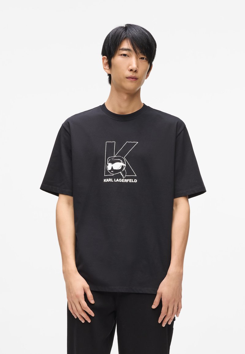 Čierne bavlnené tričko s krátkymi rukávmi, s bielou grafikou stylizovaného písmena "K" a textom "KARL LAGERFELD" pod ním.