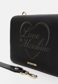 Svart handväska med präglad "Love Moschino"-logotyp i guld. Slät material, rektangulär form, dekorerad med en guldspänne och sömmar.