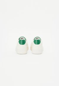 White sneakers with green leather heel accents, rounded shape, textured rubber sole, and clean design. Minimalist style with a smooth finish.