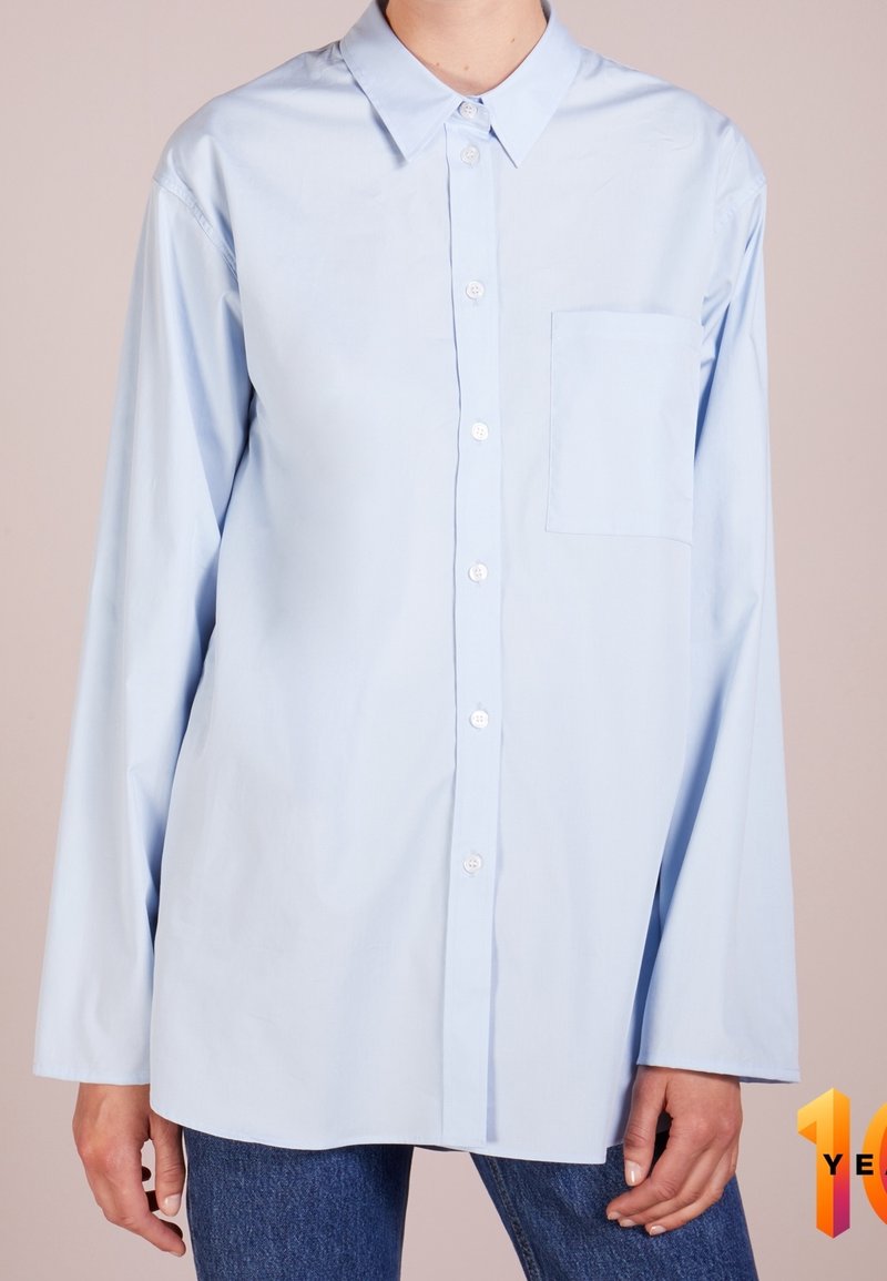 Light blue oversized long-sleeve shirt made of cotton, featuring a button-down front, a collar, and a single chest pocket.