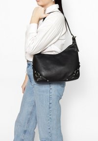 Zwarte leren schoudertas met een gestructureerd oppervlak, gebogen vorm, zilveren hardware accenten en een verstelbare schouderband.