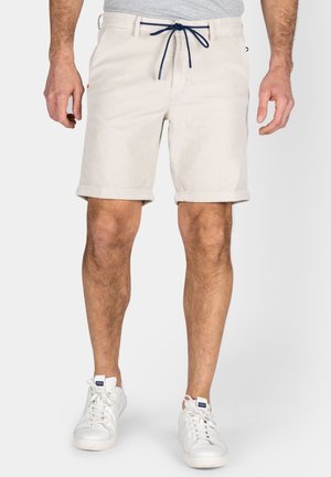 Beige shorts met opgerolde manchetten, een donkere blauwe trekkoord taille en een gestructureerde stof. Draagt met witte sneakers.