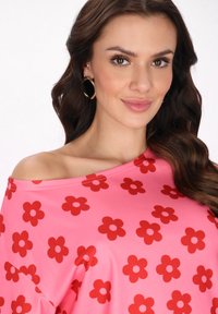 Roze top met rood bloemenpatroon, off-the-shoulder ontwerp, gladde stof, ronde halslijn en een overall losse pasvorm.