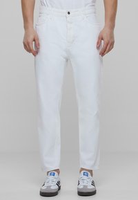 Jeans din denim alb cu o croială dreaptă, având ușoare deteriorări. Asortate cu adidași sport gri și albastru.