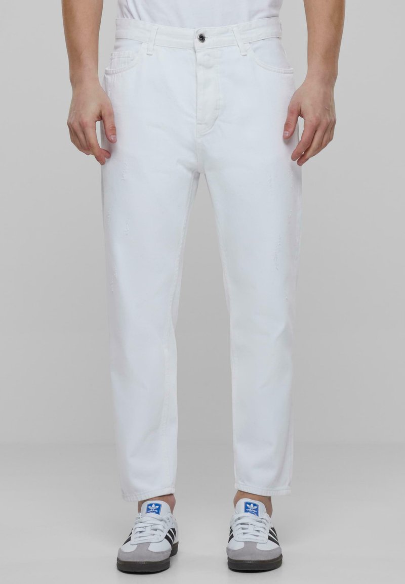 Jeans de mezclilla blanca con corte recto, con ligeros desgastes. Combinados con zapatillas deportivas grises y azules.