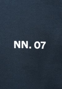 Tissu bleu foncé avec texte blanc "NN. 07" centré, montrant une texture tricotée et un lettrage clair et gras.