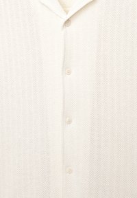 Knit cardigan in off-white with a textured fabric, featuring a shawl collar and five beige buttons down the front for closure.