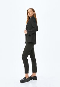 Svart rutigt blazer med slagkrage, silverfärgade knappar, kombinerat med mörka byxor och svarta loafers. Slät tyg och skräddarsydd passform.