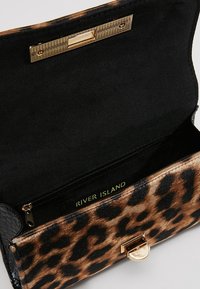 Torebka w panterkę z czarnym, teksturowanym bokiem, złotymi elementami i wewnętrzną kieszenią na zamek. Wnętrze wyłożone czarną tkaniną.