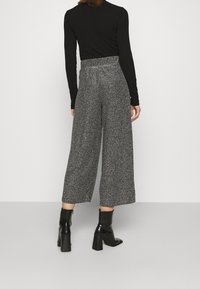 Szare spodnie o szerokich nogawkach z teksturowanym wzorem, o wysokim stanie i elastycznym pasie, zestawione z czarnymi botkami na kostkę.