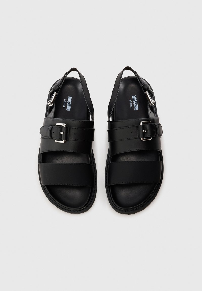 Black leather sandals with two wide straps and a buckle detail. Open back design with smooth texture and a stitched edge.