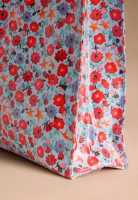 Šviesiai mėlyna gėlių raštų pirkinių rankinė, puošta raudonomis ir violetinėmis gėlėmis su žaliais lapais ir oranžinėmis žvaigždutėmis. Tekstūruotas audinys su siūtais kraštais.