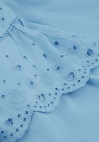 Lichtblauwe katoenen stof met ingewikkelde borduursels van schelp patronen, hartvormige uitsneden en golvende randen. Zachte textuur.