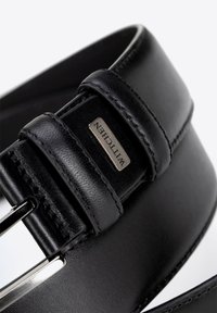 Cintura in pelle nera con finitura liscia, dotata di una fibbia in metallo argentato e un'etichetta rettangolare del marchio. Dettagli cuciti lungo i bordi.