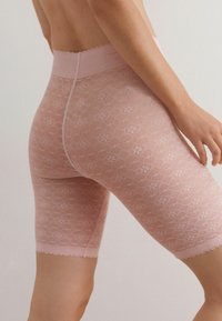 Rosa spetsshorts med blommönster, vågig nederkant och bred midjeresår. Tyget är genomskinligt och visar en delikat textur.