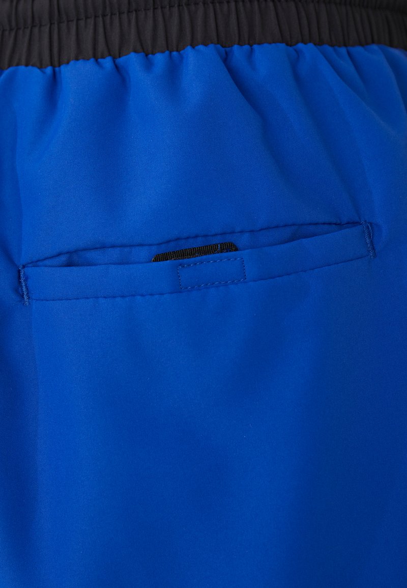 Pantalones cortos azules con una cinturilla elástica negra, que presentan un pequeño bolsillo horizontal en la parte trasera con un forro de tela negra. Textura suave.