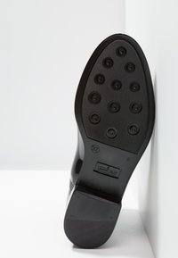 Semelle en caoutchouc noir avec des éléments de traction circulaires, un motif en relief et un logo embossé. Forme effilée avec une finition lisse et brillante. Taille 37.