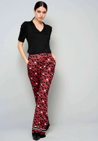 Zwarte T-shirt met korte mouwen en V-hals, gecombineerd met rode broek met patroon en zwarte en witte vormen. De broek heeft een slim fit en zakken.