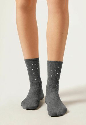 Grå bomullssockor med ett ribbat skaft, prydda med ett mönster av vita prickar. Mjuk textur och standard längd för ankelsockor.