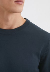 Marineblauer Rundhalsausschnitt-Pullover aus glattem Stoff, mit geripptem Kragen und Bündchen sowie dezenten Nähte an den Schultern.
