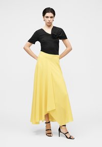 Μαύρο τοπ με λεπτομέρεια δεμένου κόμπου, συνδυασμένο με μια αέρινη κίτρινη φούστα με ασύμμετρο τελείωμα. Μαύρα σανδάλια με τακούνι ολοκληρώνουν το σύνολο.