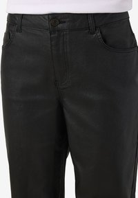 Μαύρο παντελόνι denim με επένδυση, με κουμπί στο μπροστινό μέρος και τσέπες, φορεμένο με ένα λευκό τοπ με ριμπ υφή που φαίνεται στη μέση.