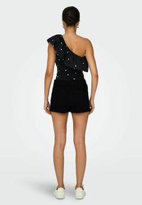 Haut noir à une épaule avec un volant et des pois blancs, associé à un short noir taille haute et des baskets blanches. Texture de tissu lisse.