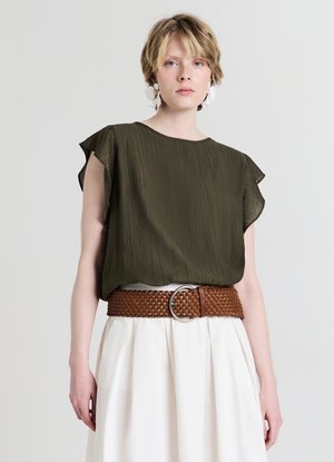 Top verde oliva a maniche corte con finitura strutturata, abbinato a una cintura larga marrone intrecciata con fibbia circolare in argento, abbinato a una gonna bianca.