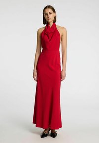 Abito rosso con maniche a halter, scollatura drappeggiata, corpetto aderente e gonna a forma di A. Realizzato in tessuto testurizzato, presenta un design lungo.